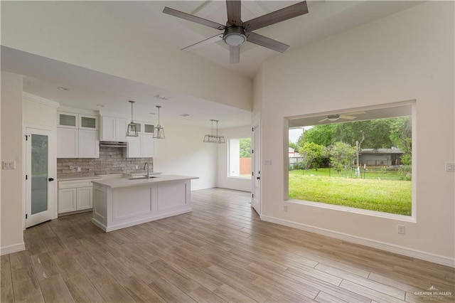 kitchen with decorative light fixtures, white cabinetry, decorative backsplash, a center island with sink, and light wood-type flooring