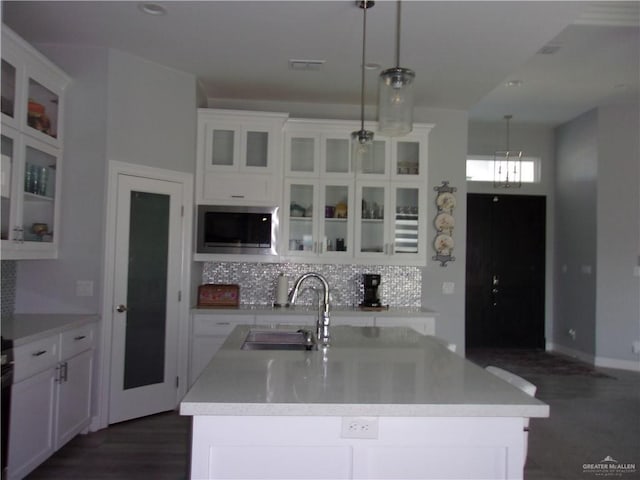 kitchen with sink, hanging light fixtures, an island with sink, decorative backsplash, and white cabinets