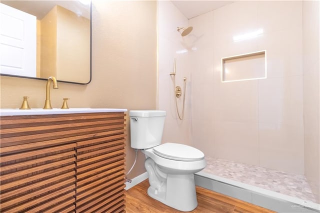 bathroom with hardwood / wood-style flooring, toilet, vanity, and tiled shower