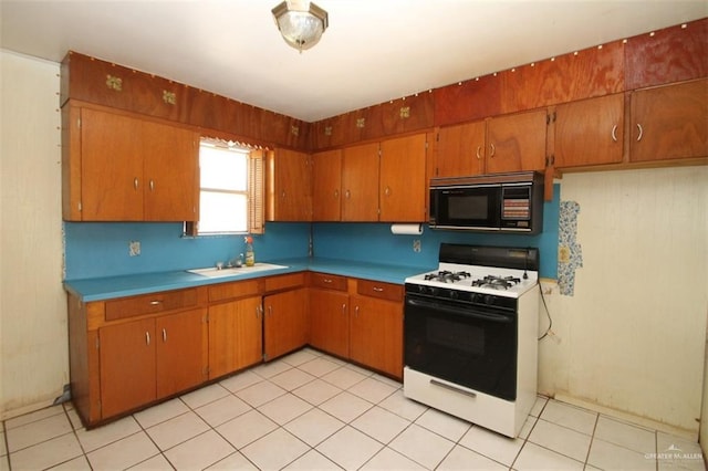 kitchen featuring black microwave, white gas stove, a sink, light countertops, and brown cabinetry