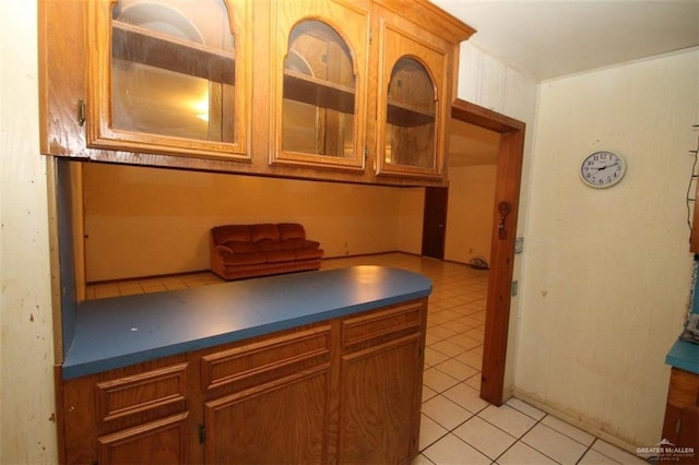 kitchen featuring light tile patterned floors, glass insert cabinets, and brown cabinets