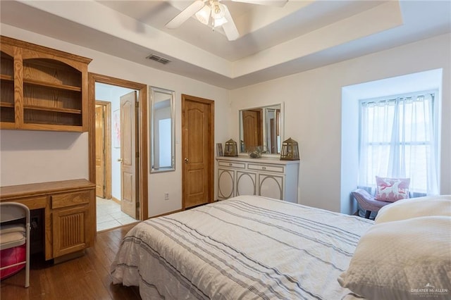 bedroom with a tray ceiling, ceiling fan, and light wood-type flooring