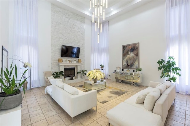 living room with a raised ceiling, a fireplace, a high ceiling, and an inviting chandelier