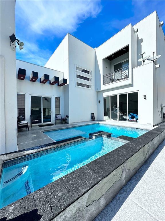 rear view of house with a balcony, a pool with connected hot tub, a patio, and stucco siding