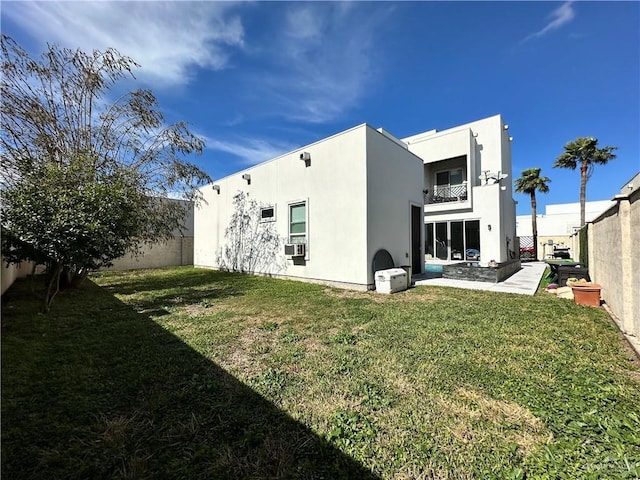 back of house with a fenced backyard, a lawn, a balcony, and stucco siding