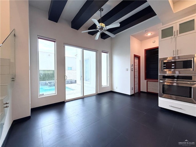 kitchen featuring a healthy amount of sunlight, baseboards, white cabinets, and beam ceiling