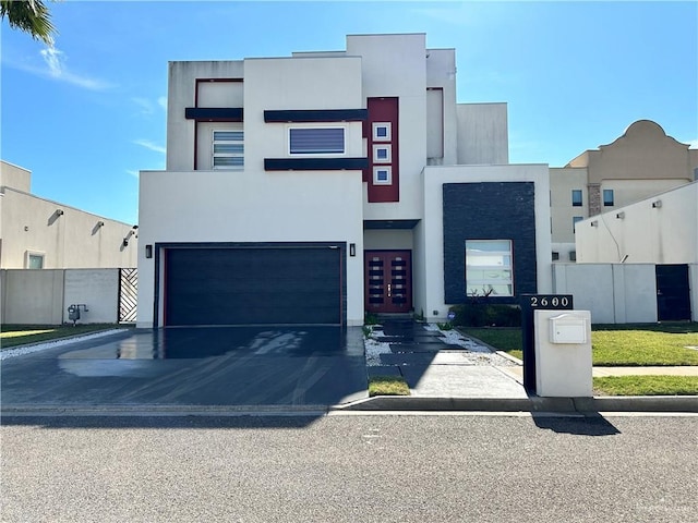 contemporary home with a garage, driveway, fence, and stucco siding