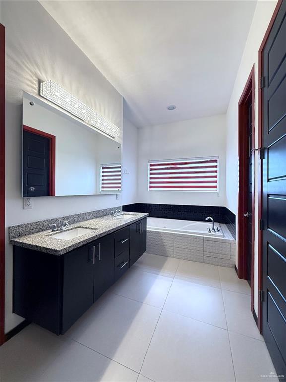 bathroom featuring tile patterned flooring, double vanity, a sink, and a bath