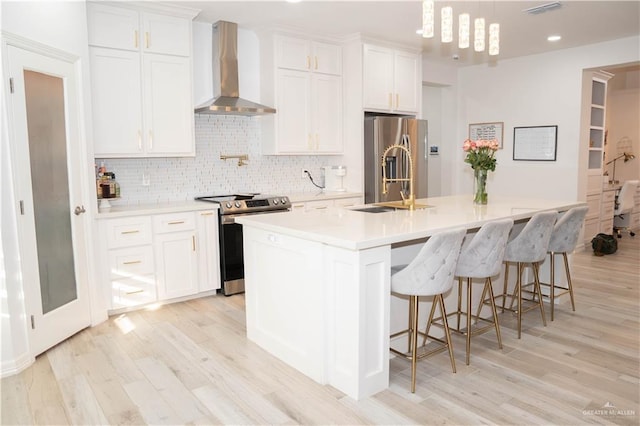 kitchen featuring a kitchen island with sink, white cabinetry, stainless steel appliances, and wall chimney exhaust hood