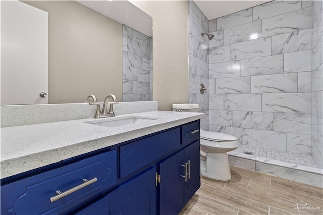 full bathroom featuring toilet, wood finish floors, a tile shower, and vanity
