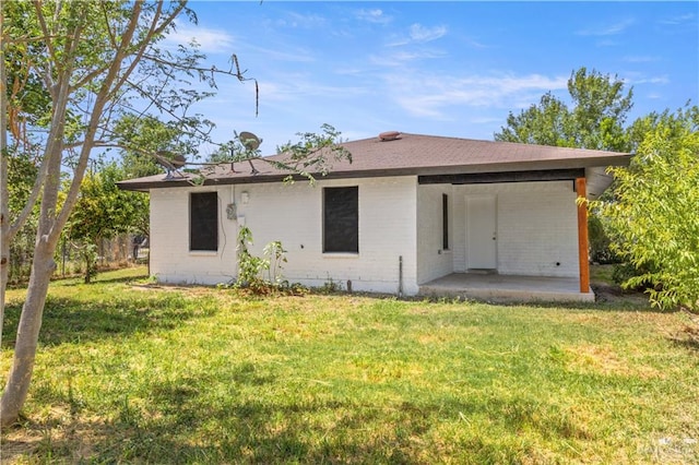 back of house featuring a lawn, brick siding, a shingled roof, and a patio area