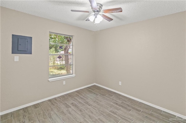 spare room featuring baseboards, electric panel, a ceiling fan, and light wood finished floors
