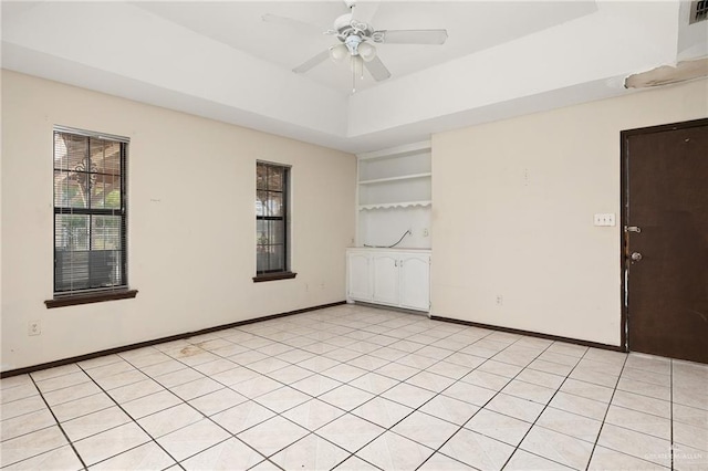 unfurnished room featuring a raised ceiling, built in features, ceiling fan, and light tile patterned flooring