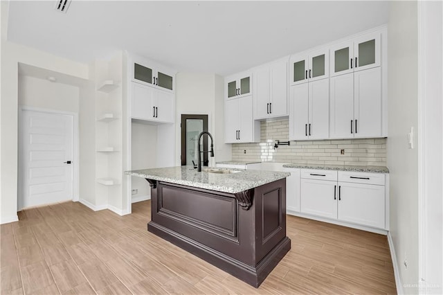 kitchen featuring a breakfast bar, sink, a center island with sink, light stone countertops, and white cabinets