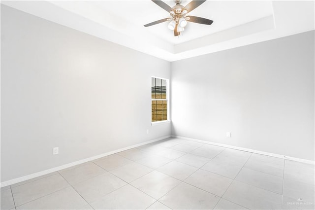 spare room featuring a tray ceiling, ceiling fan, and light tile patterned flooring