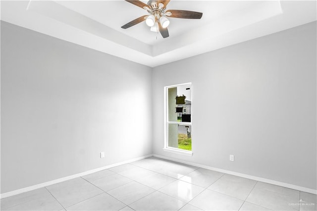 spare room with a tray ceiling, ceiling fan, and light tile patterned floors