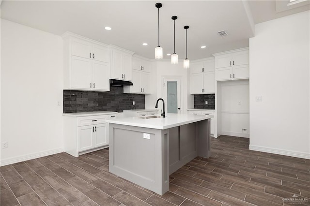 kitchen with white cabinetry, sink, dark wood-type flooring, an island with sink, and decorative light fixtures