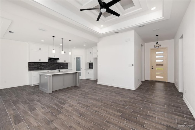 kitchen with white cabinetry, hanging light fixtures, dark hardwood / wood-style floors, an island with sink, and decorative backsplash