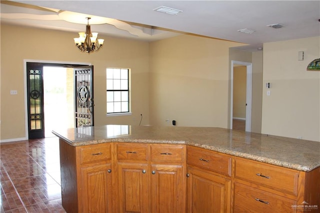 kitchen with light stone countertops, pendant lighting, dark tile patterned floors, and a notable chandelier