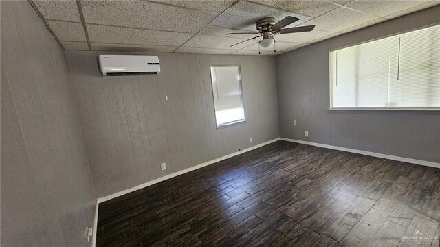 spare room featuring a paneled ceiling, dark hardwood / wood-style floors, a wall unit AC, and a healthy amount of sunlight