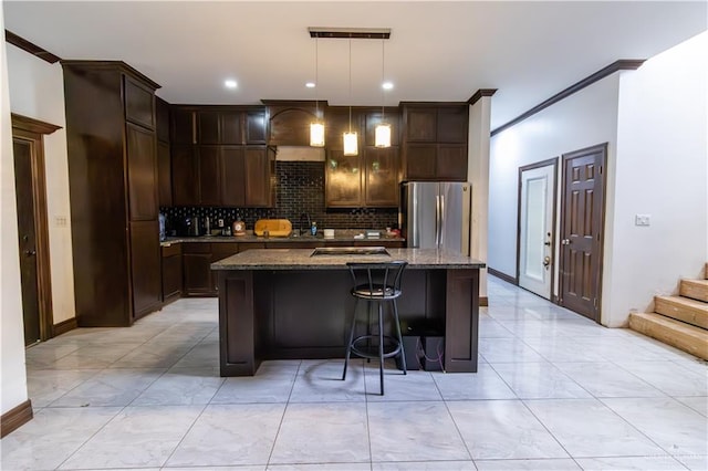 kitchen featuring decorative light fixtures, stainless steel fridge, dark stone countertops, and a kitchen island with sink