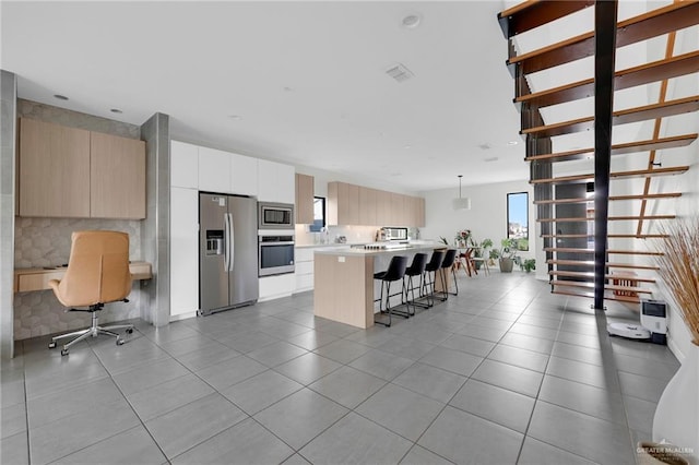 kitchen with appliances with stainless steel finishes, light countertops, a kitchen breakfast bar, a center island, and modern cabinets