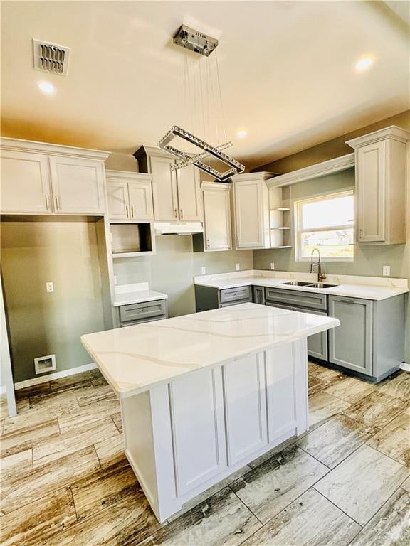 kitchen featuring sink, a kitchen island, light stone counters, pendant lighting, and white cabinets