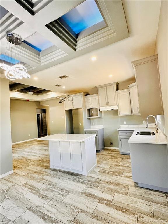 kitchen with white cabinetry, sink, coffered ceiling, decorative light fixtures, and a kitchen island