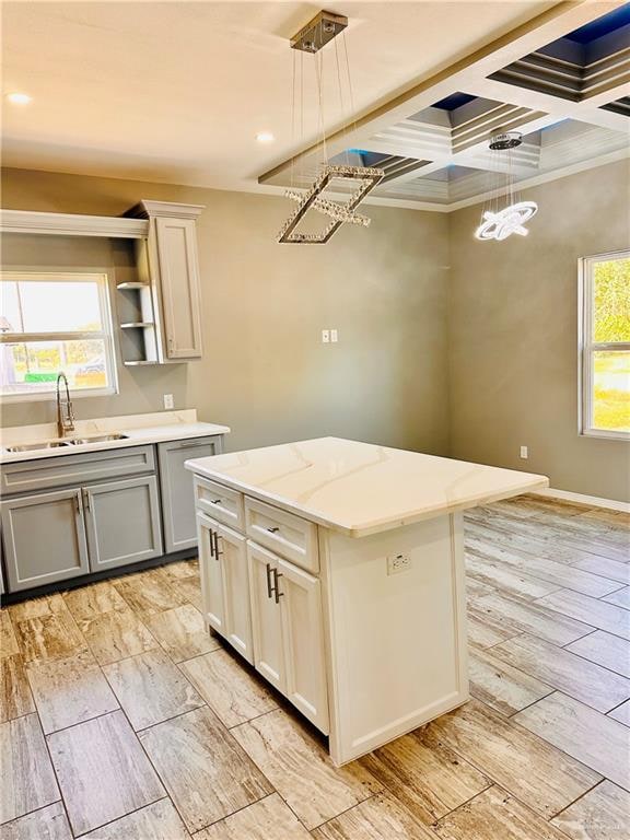 kitchen with light stone counters, coffered ceiling, sink, pendant lighting, and a center island