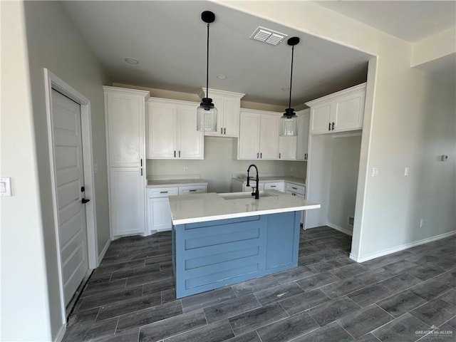 kitchen featuring white cabinets, sink, hanging light fixtures, and a center island with sink