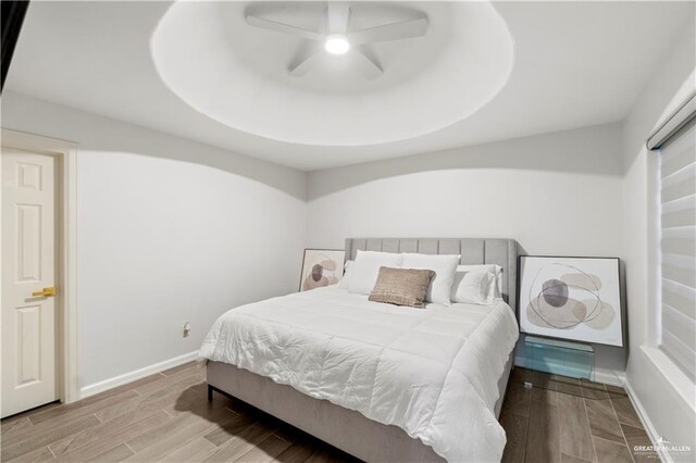 bedroom with ceiling fan, a raised ceiling, and light wood-type flooring