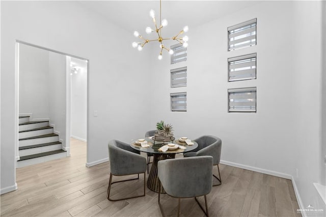 dining area with a towering ceiling, light hardwood / wood-style floors, and a notable chandelier