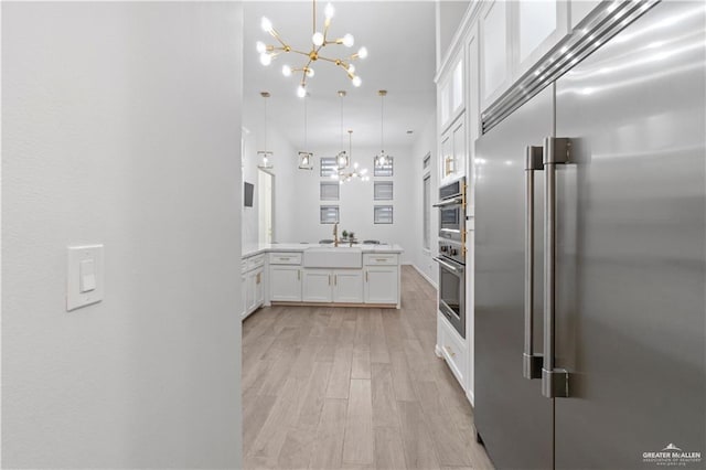 kitchen with an inviting chandelier, white cabinets, light hardwood / wood-style flooring, built in refrigerator, and decorative light fixtures