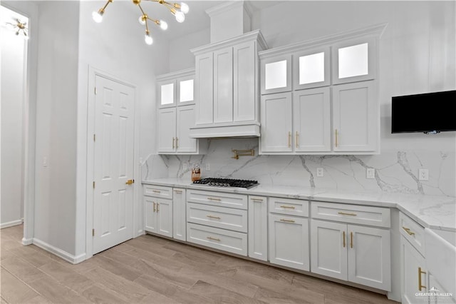 kitchen with decorative backsplash, light stone counters, stainless steel gas cooktop, light hardwood / wood-style flooring, and white cabinetry