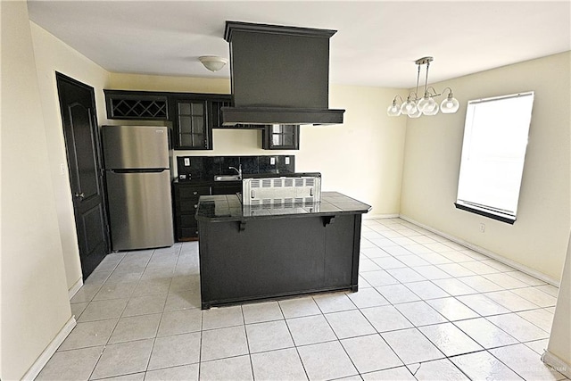 kitchen featuring stainless steel refrigerator, an inviting chandelier, pendant lighting, a kitchen bar, and custom exhaust hood