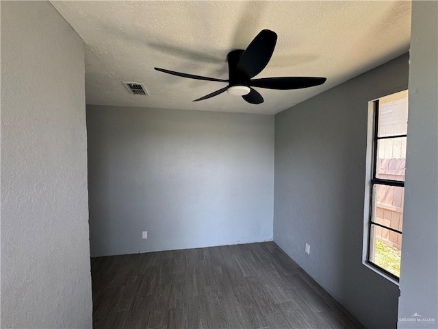 spare room featuring plenty of natural light, visible vents, dark wood-style flooring, and a ceiling fan