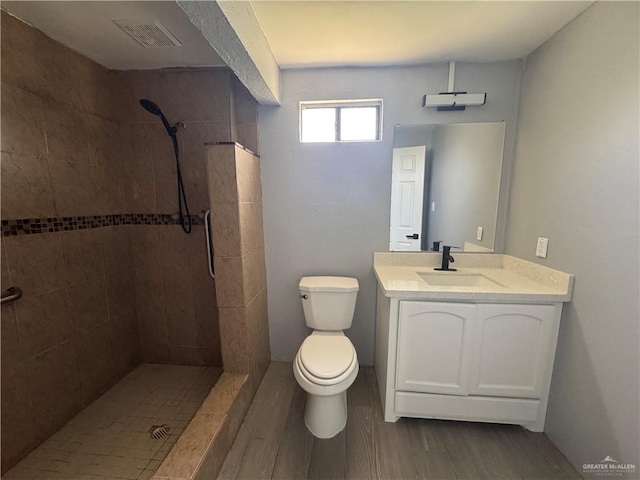 full bathroom featuring vanity, toilet, visible vents, tiled shower, and wood finished floors