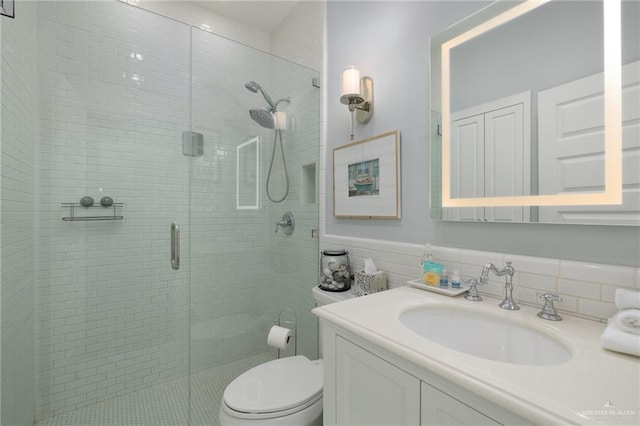 bathroom featuring vanity, toilet, a shower with door, and tile walls