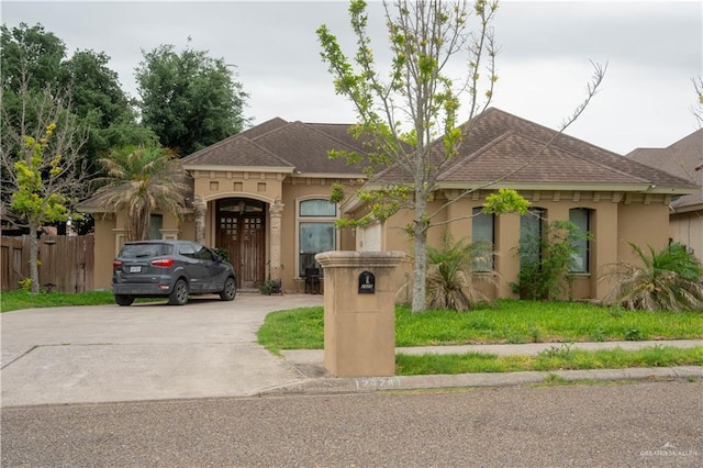 mediterranean / spanish home featuring a shingled roof, fence, stucco siding, and concrete driveway