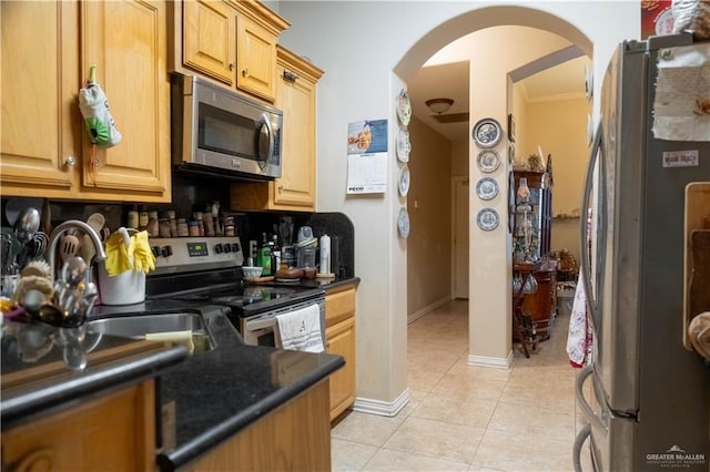 kitchen with dark countertops, stainless steel appliances, arched walkways, light tile patterned flooring, and backsplash