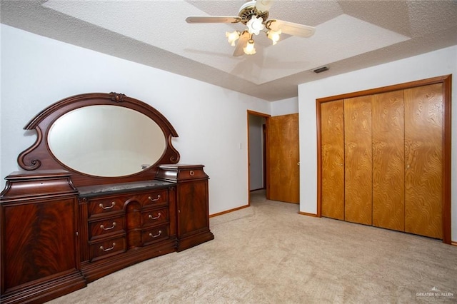 bedroom featuring ceiling fan, a closet, light carpet, and a textured ceiling