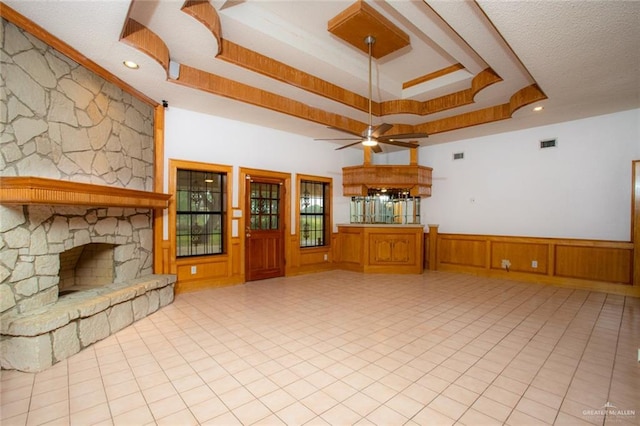 unfurnished living room with a textured ceiling, a fireplace, ceiling fan, and a tray ceiling