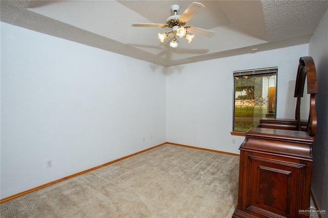 carpeted spare room with a textured ceiling, ceiling fan, and a tray ceiling