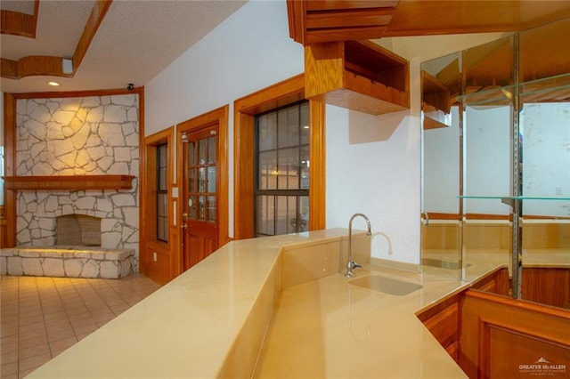 kitchen featuring sink, a stone fireplace, a textured ceiling, and light tile patterned floors