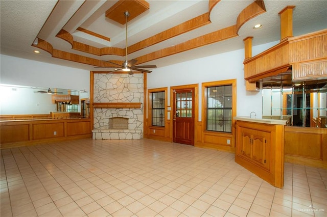 unfurnished living room with ceiling fan, a stone fireplace, wooden walls, and a tray ceiling