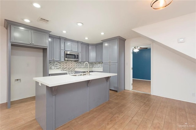 kitchen featuring decorative backsplash, gray cabinetry, a kitchen island with sink, and a kitchen bar