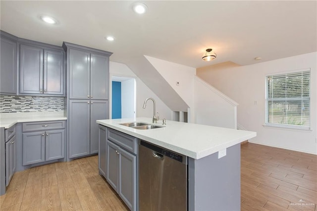 kitchen featuring dishwasher, sink, backsplash, gray cabinets, and a kitchen island with sink