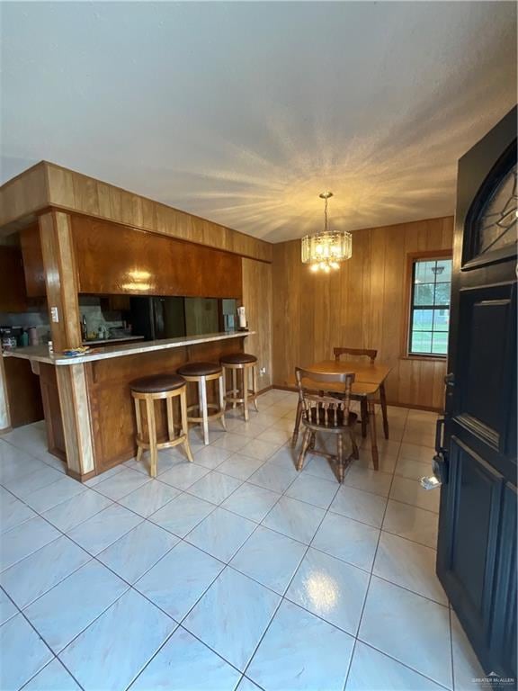 tiled dining room with wooden walls and a notable chandelier