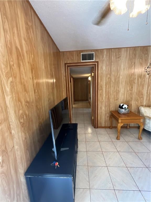 hallway featuring wood walls, light tile patterned floors, and a textured ceiling