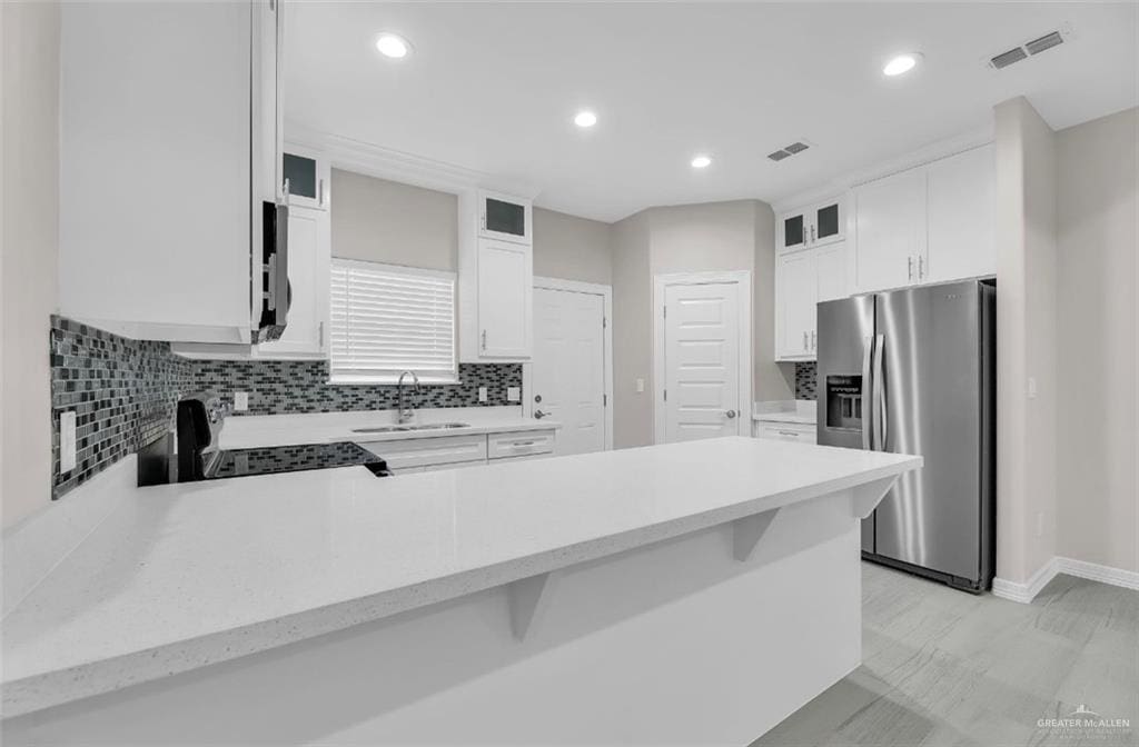 kitchen featuring kitchen peninsula, stainless steel refrigerator with ice dispenser, sink, black range, and white cabinets